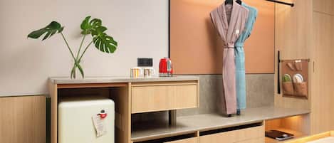 A modern kitchen with a built-in refrigerator, wooden cabinets, a hanging robe, and a plant.