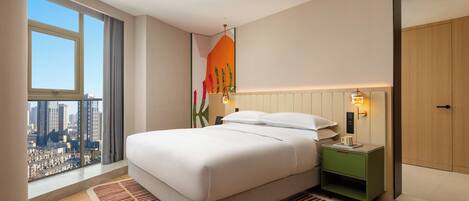 A modern hotel room with a large bed, a nightstand, a green side table, a city view, and a large window.