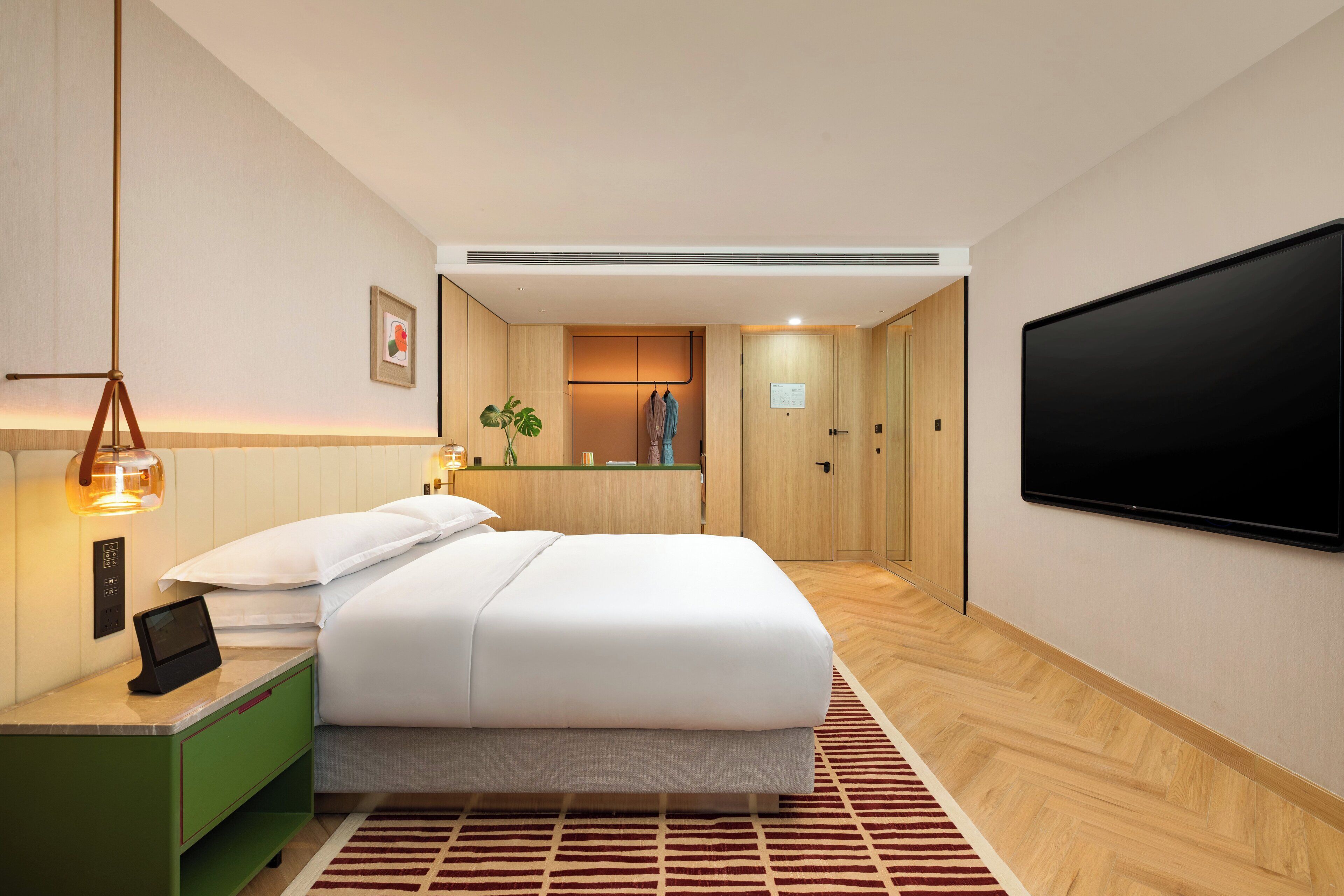 Ein modernes Hotelzimmer mit Bett, Nachttisch, Fernseher und Blick auf den Flur.