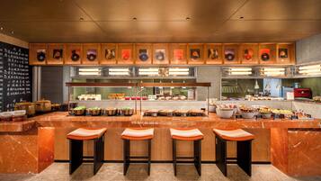 A modern kitchen with marble countertops, wooden bar stools, and a variety of food items displayed on the counter.
