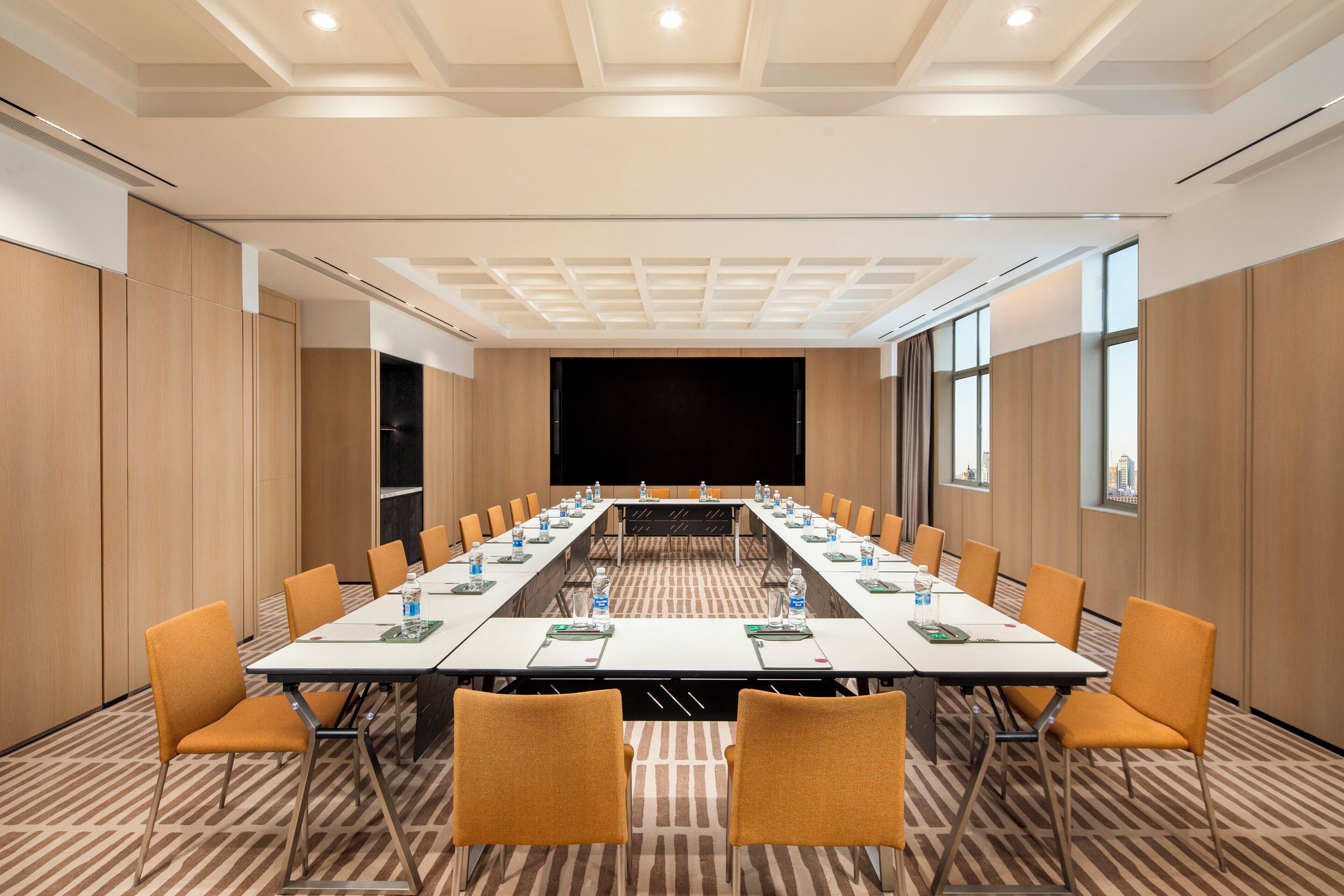 A conference room with a long table, chairs, and a screen at the front.
