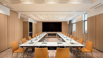 A conference room with a long table, chairs, and a screen at the front.