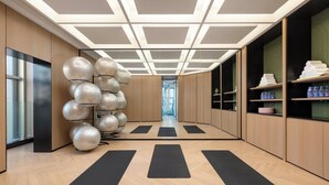 Un gimnasio moderno con equipo de ejercicio, colchonetas negras, pisos de madera e iluminación empotrada en el techo.