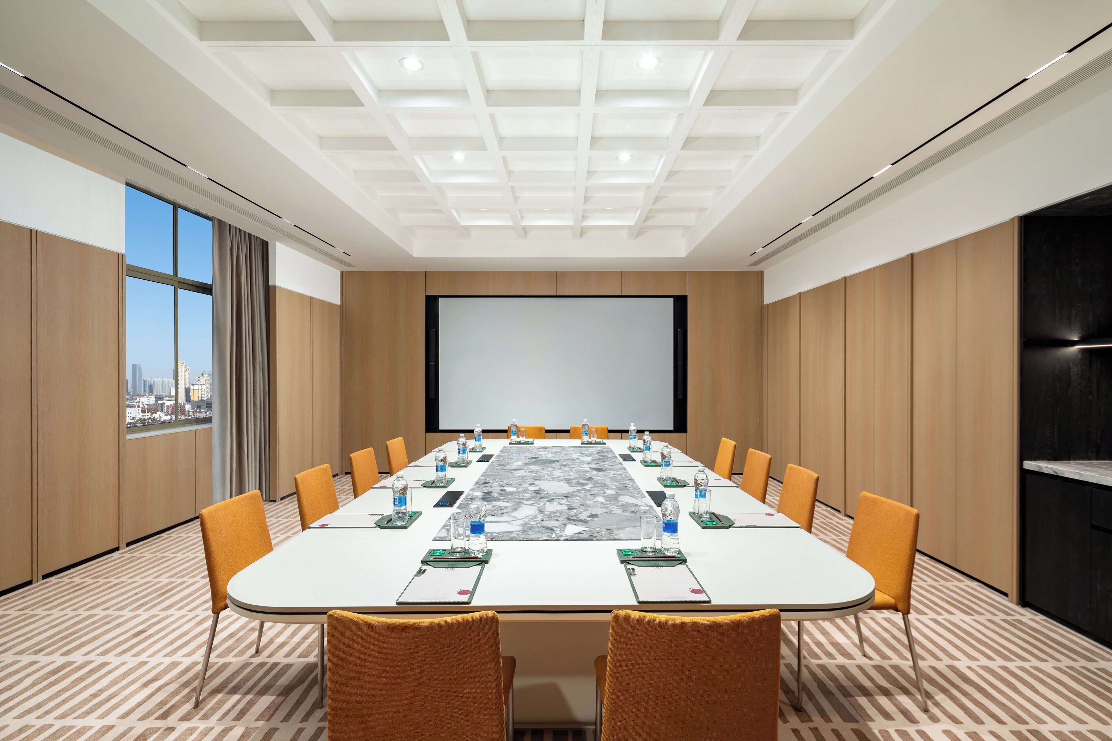 Une salle de conférence équipée d’une grande table, de chaises, d’un écran de projection et offrant une vue sur la ville grâce à de grandes fenêtres.