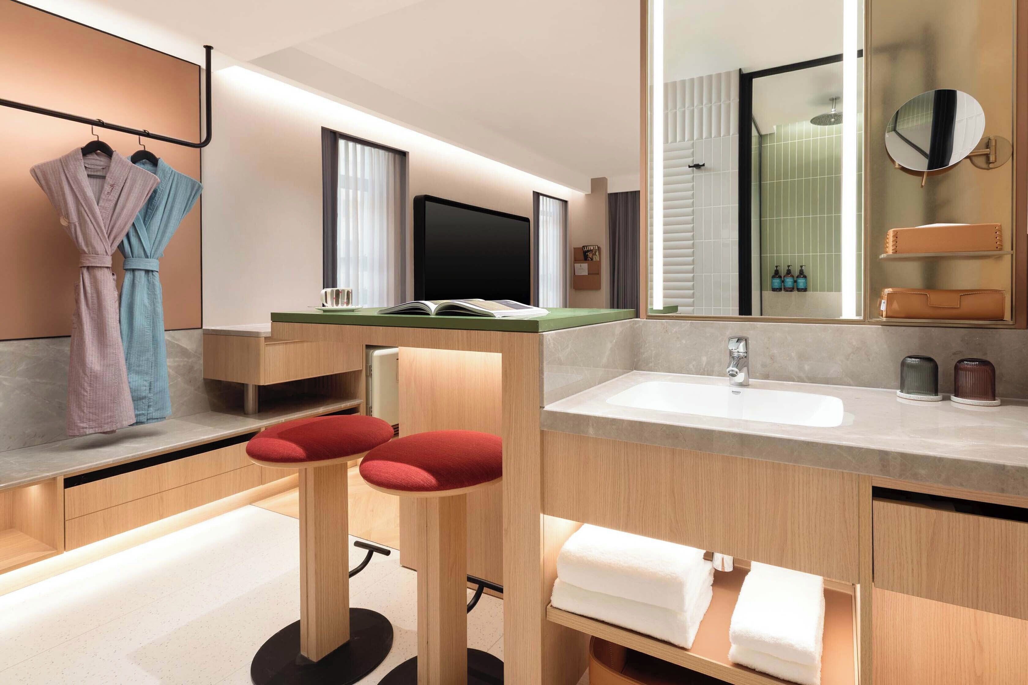 A modern bathroom with a large mirror, a sink, and two red cushioned stools.