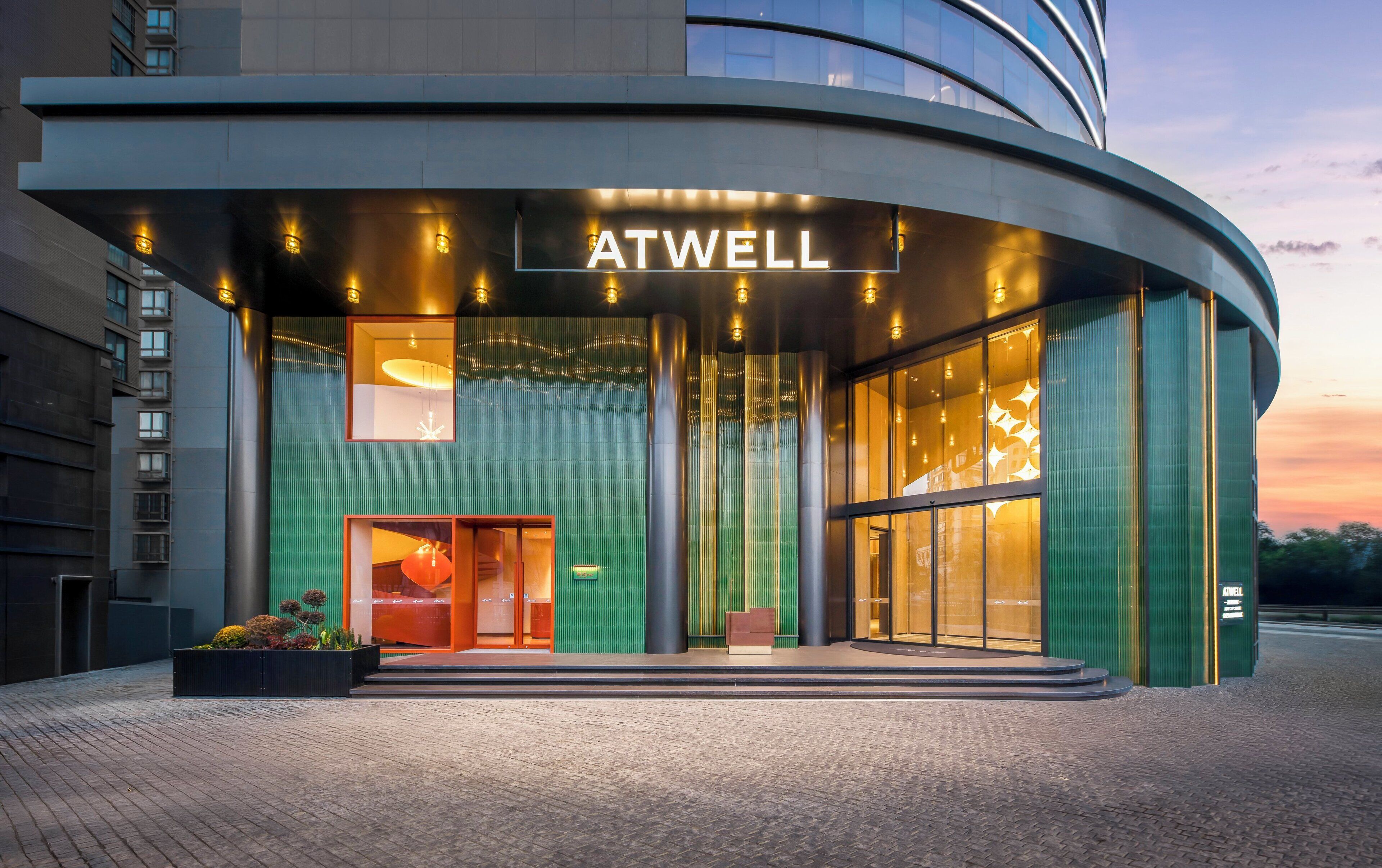 Una entrada de hotel moderna con fachada curva, señalización ATWELL y un área de acceso bien iluminada.