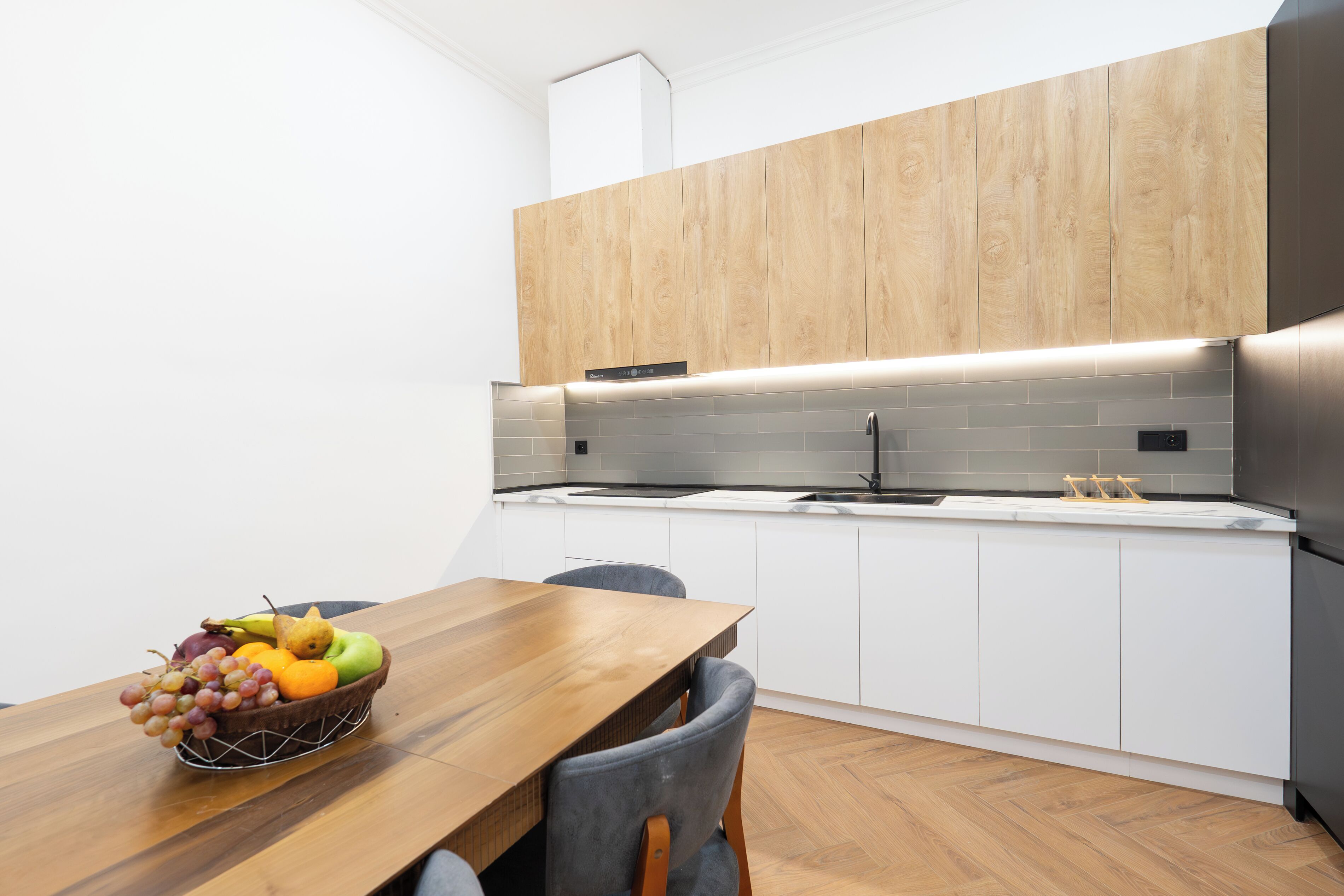 A modern kitchen with white cabinets, a wooden countertop, and a dining table with a fruit bowl.