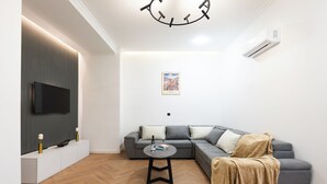 A modern living room with a grey sectional sofa, a round coffee table, a mounted TV, and a wall-mounted air conditioner. - Chic & Modern 4BR Home in Old Tbilisi (Tbilisi)