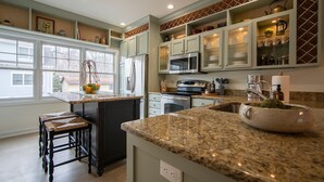 A kitchen with granite countertops, a refrigerator, a microwave, and a sink. There are two bar stools and a window with a view of the outside. - Downtown Saugatuck Dream (Saugatuck)