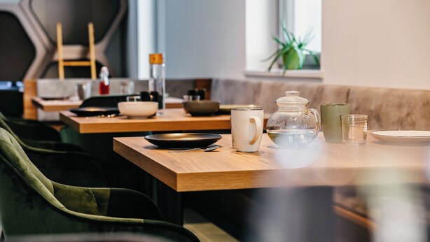 A dining area with wooden tables, chairs, and various tableware including bowls, cups, and a teapot. - Nature House (Brennero)