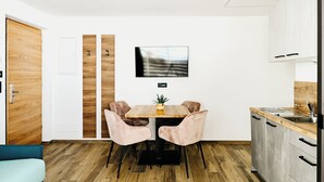 A modern kitchen with a wooden dining table, two pink chairs, and a TV mounted on the wall. - Nature House (Brennero)