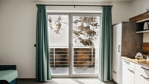 A modern kitchen with white cabinets, a wooden countertop, and a sliding glass door leading to a balcony with a view of trees and snow. - Nature House (Brennero)