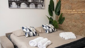 A modern bedroom with a bed, a sofa, a large plant, and a cityscape painting on the wall. - Maison Monteverde/ Trastevere (Roma)