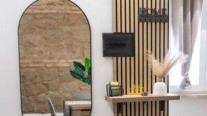 A modern room with a stone wall, wooden slat partition, a round mirror, a bench, a small table with a remote control, and a plant. - Maison Monteverde/ Trastevere (Roma)