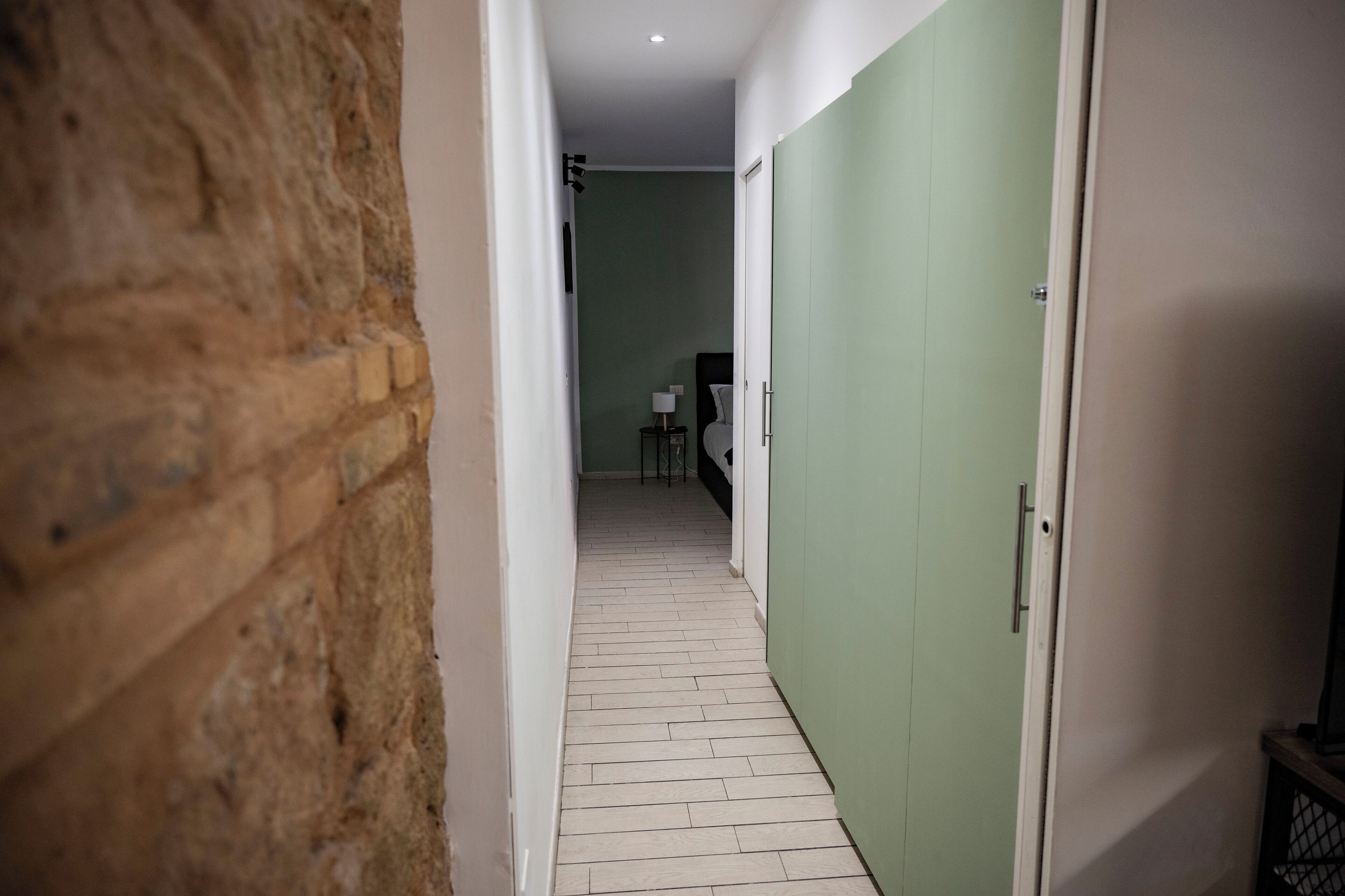 Un pasillo estrecho con una pared de ladrillo a un lado y una puerta verde al otro.