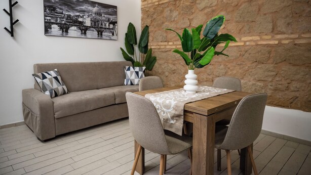 A living room with a sofa, dining table, chairs, and a large plant. - Maison Monteverde/ Trastevere (Roma)