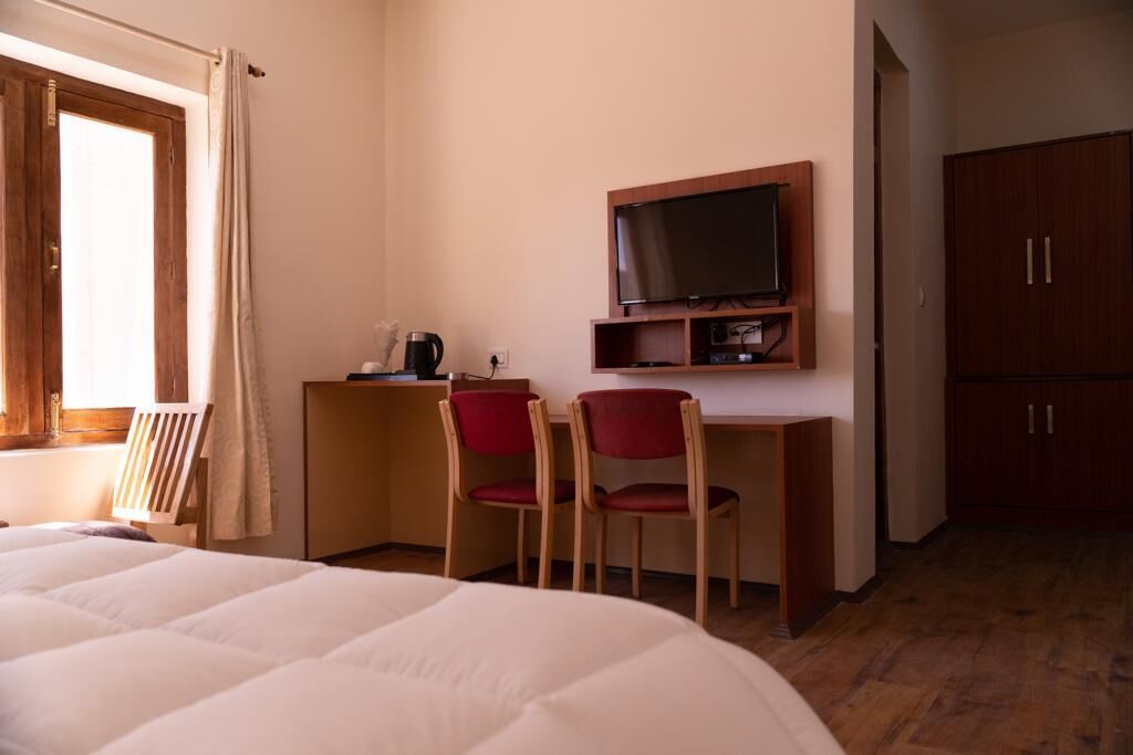 Une chambre d’hôtel comprenant un lit, un bureau avec une télévision, deux chaises et une armoire.