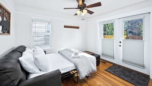 Une pièce de taille modeste comprenant un lit, un canapé, un ventilateur de plafond et une porte donnant sur un balcon.