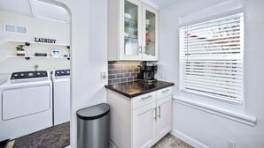 Un espace buanderie comprenant un lave-linge, un meuble avec des portes en verre et une fenêtre avec des stores.