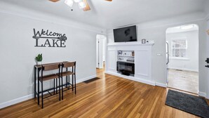 Un salon moderne avec un plancher en bois, un ventilateur de plafond, une cheminée et un téléviseur fixé au-dessus.