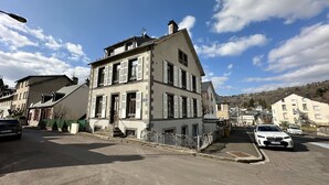 Ein mehrstöckiges Gebäude mit einer symmetrischen Fassade, großen Fenstern mit Fensterläden und einer sichtbaren Treppe, die zum Eingang führt.