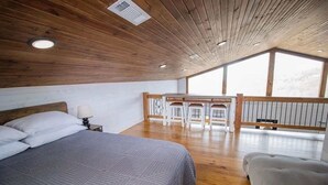 A bedroom with a large bed, a wooden ceiling, and a balcony with a table and chairs. - Ozark Escape - Hot Tub, Mountain Views, Near River (Compton)