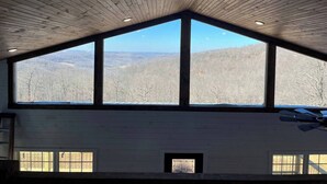 A high-ceilinged room with large windows offering a view of a forested landscape. - Ozark Escape - Hot Tub, Mountain Views, Near River (Compton)