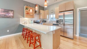 A modern kitchen with a central island, wooden cabinets, stainless steel appliances, and pendant lighting. - Razorback Retreat – Walk to Stadium & Downtown (Fayetteville)