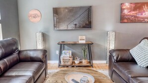 A living room with two leather sofas, a coffee table, a side table with a flower market basket, and two wall-mounted picture frames. - Razorback Retreat – Walk to Stadium & Downtown (Fayetteville)