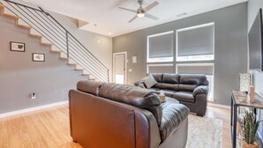 A modern living room with a staircase, leather sofas, and a ceiling fan. - Razorback Retreat – Walk to Stadium & Downtown (Fayetteville)