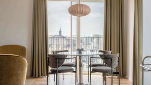 Un espace repas avec une table ronde et des chaises, un luminaire suspendu et une vue sur le paysage urbain grâce à de grandes fenêtres.