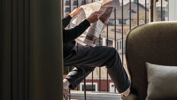 A person reading a newspaper on a balcony with a view of buildings and a church steeple. - Clover House 2BR by Daniel&Jacob's (København)