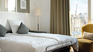 A hotel room with a bed, a chair, a lamp, a window with curtains, and a view of buildings. - Clover House 2BR by Daniel&Jacob's (København)