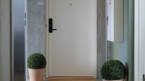 A hallway with a white door, two potted plants, a light switch, and a thermostat on the wall. - Clover House 2BR by Daniel&Jacob's (København)