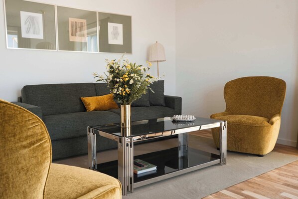 A modern living room with a grey sofa, a yellow armchair, and a glass coffee table with a vase of flowers.