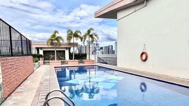 A rooftop swimming pool with a clear view of the city skyline, surrounded by palm trees and a brick wall. - BGC McKinley Center Prime Accommodations (Taguig)