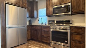 Une cuisine avec des meubles en bois, des appareils électroménagers en acier inoxydable et une fenêtre équipée de stores.