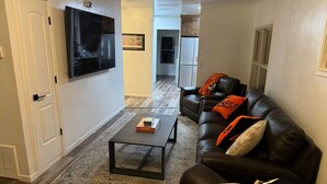 Un salon avec un canapé en cuir noir, une table basse et un téléviseur à écran plat fixé au mur.
