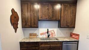 A kitchen with wooden cabinets, a granite countertop, a stainless steel sink, and a dishwasher. - 2 King Bed OSU Rental House (Stillwater)