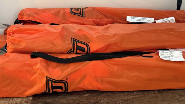 Three orange bags with black handles and a logo, placed on a wooden surface. - 2 King Bed OSU Rental House (Stillwater)