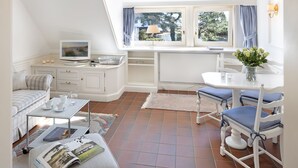 Una habitación acogedora con una cama, una mesita con televisor, un rincón de comedor con sillas y una ventana con cortinas.