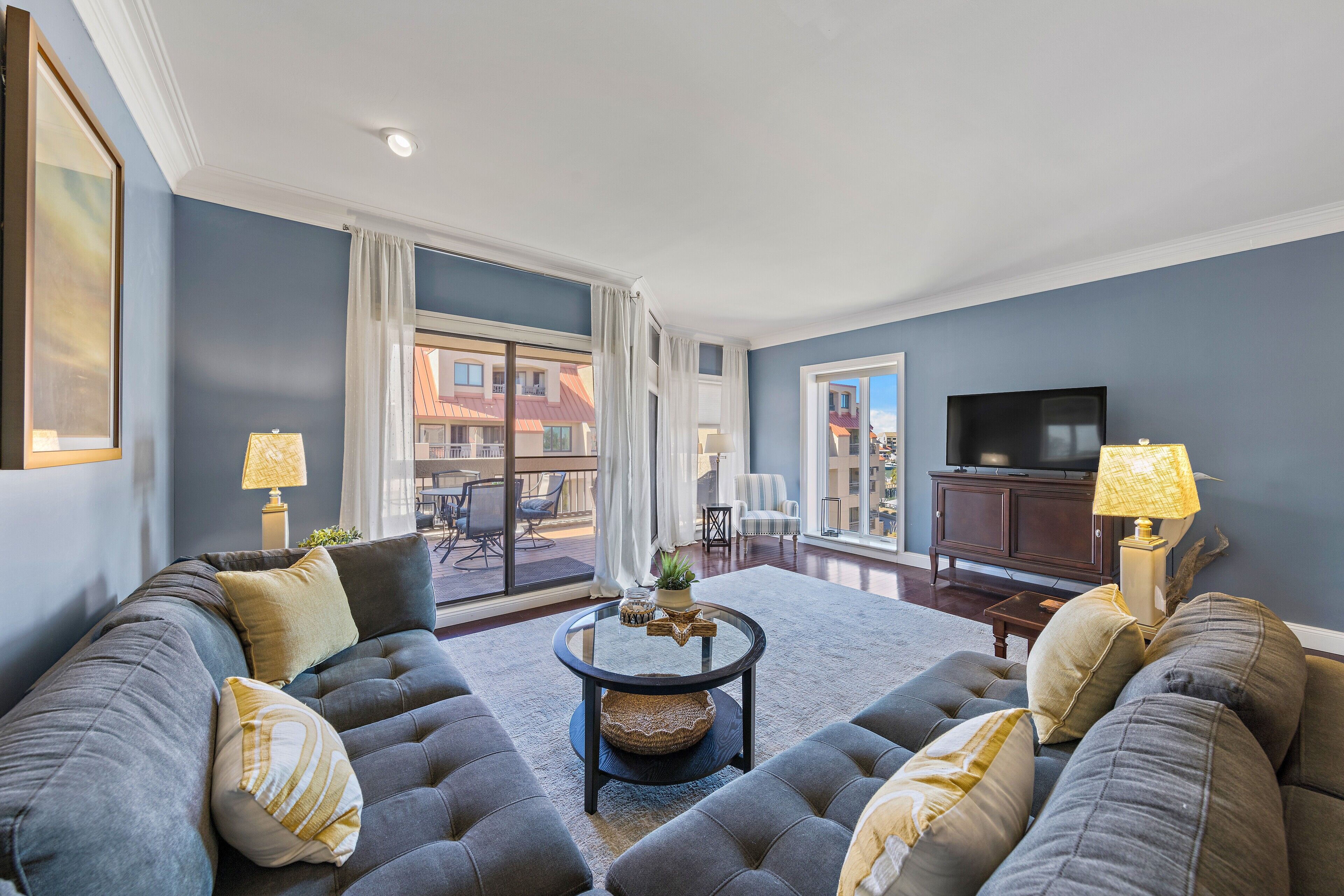 A living room with a large gray sectional sofa, a glass coffee table, and a flat-screen TV.
