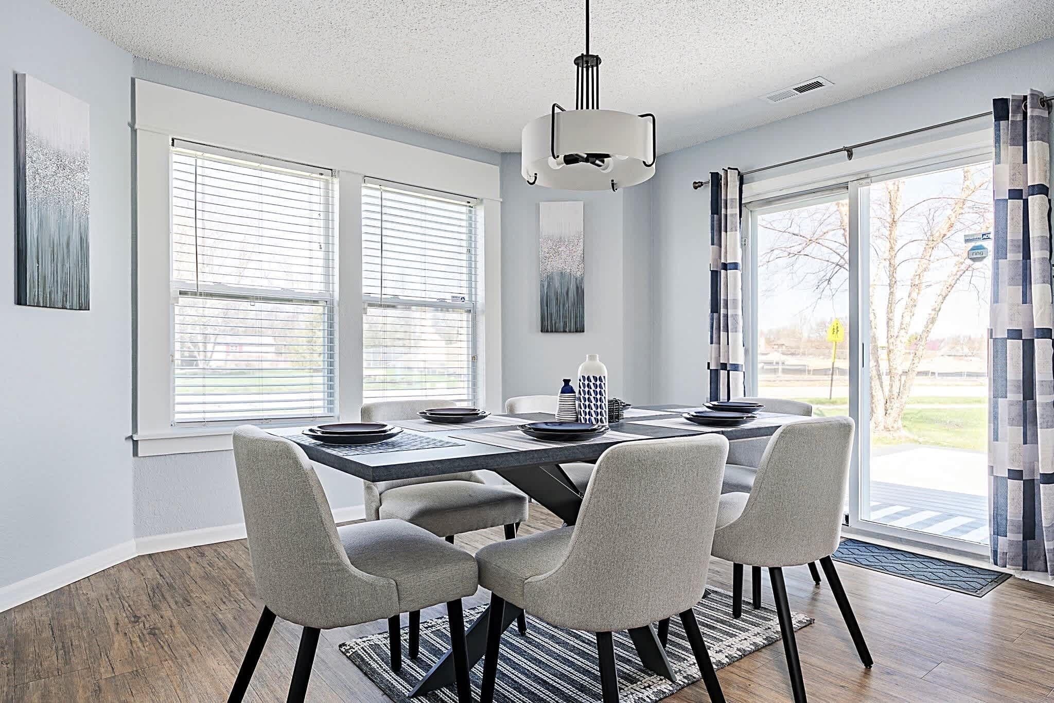 Un espace repas moderne avec une table rectangulaire, six chaises grises et un luminaire suspendu.