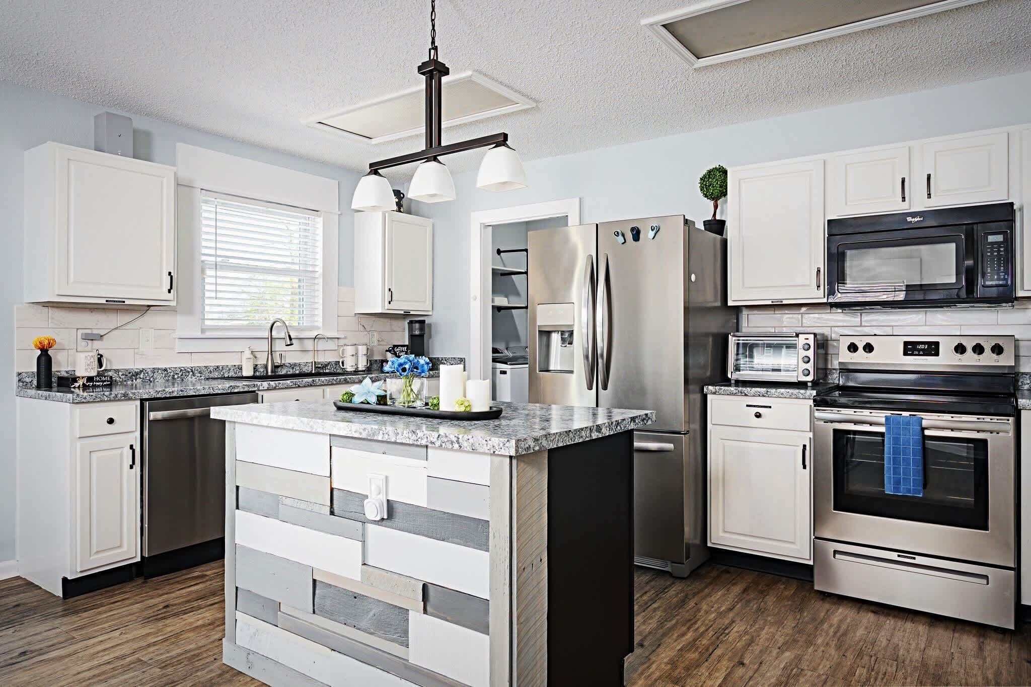 A modern kitchen with white cabinetry, stainless steel appliances, a central island, and a pendant light fixture.
