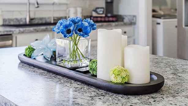 A kitchen counter with a tray holding a vase with blue flowers, white candles, and green flowers. - The Cozy Charcoal Cottage | Garage | Grill & Patio (Brownsburg)