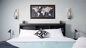 A neatly made bed with a world map artwork above it, two wall-mounted lamps, and a small plant on the nightstand. - The Cozy Charcoal Cottage | Garage | Grill & Patio (Brownsburg)
