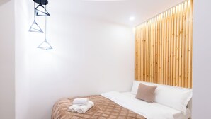 A modern hotel room with a wooden headboard, a neatly made bed with a patterned bedspread, and a set of geometric pendant lights.