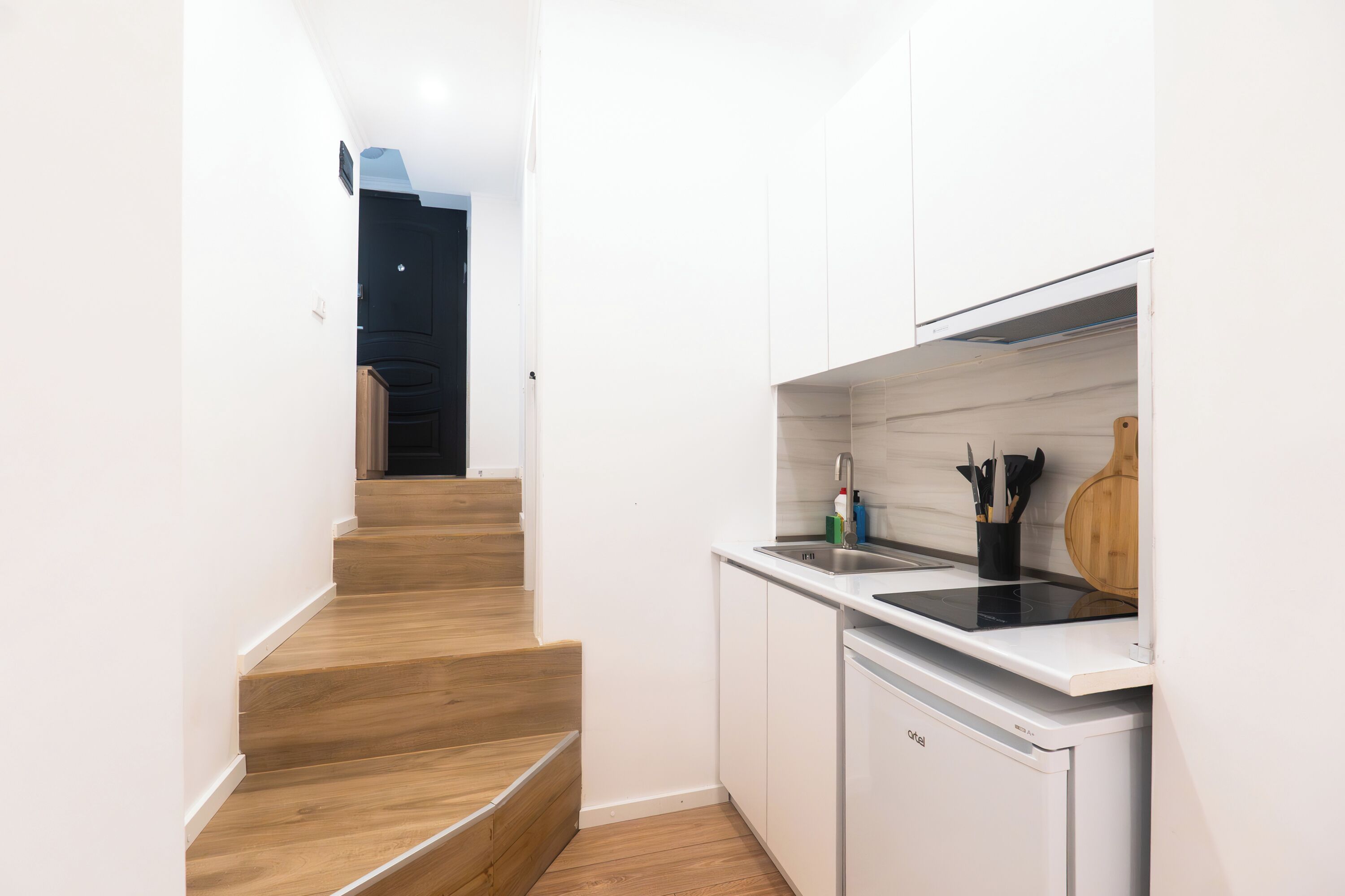 Una cocina moderna con armarios blancos, una escalera de madera y un lavavajillas empotrado.