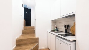 A modern kitchen with white cabinets, a wooden staircase, and a built-in dishwasher.