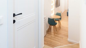 A hallway with a white door, wooden flooring, and a dining area with green chairs and a table.